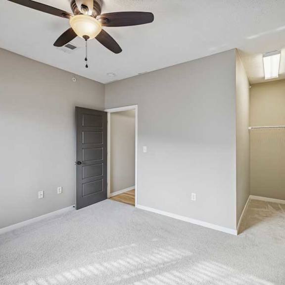 Thumbnail 15 of 22 A carpeted bedroom with a ceiling fan and open walk-in closet space.