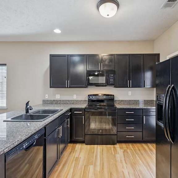 Thumbnail 7 of 22 A kitchen with dark wooden cabinets, granite countertops, and black applainces.