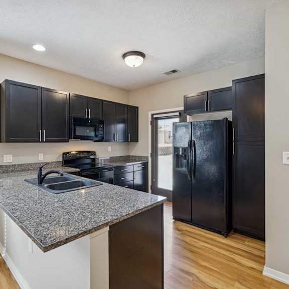 Thumbnail 8 of 22 A kitchen with dark wooden cabinets, granite countertops, and black-finish appliances.