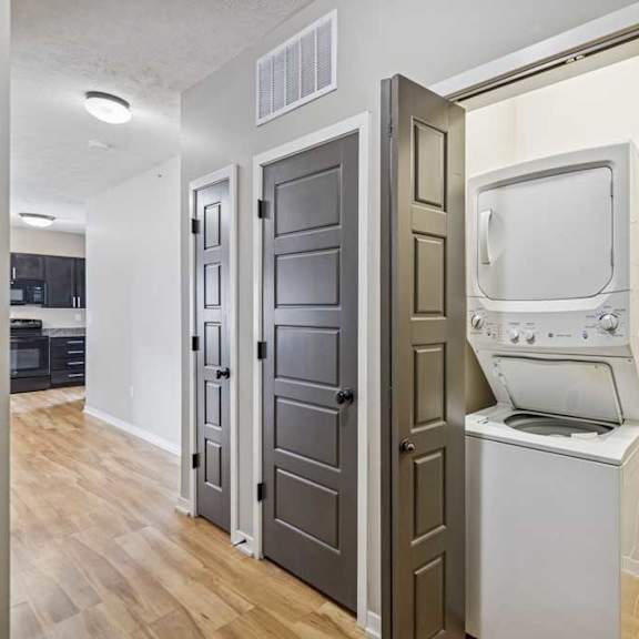 Thumbnail 19 of 22 A hallway with multiple closets, and an open closet with a stacked washer and dryer with built-in shelving next to it.