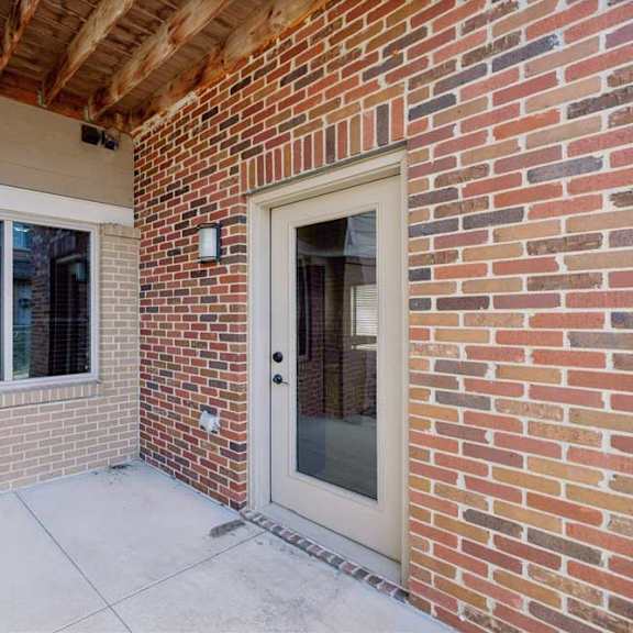 Thumbnail 9 of 22 A red brick apartment building with a covered patio, and a large window from a bedroom.