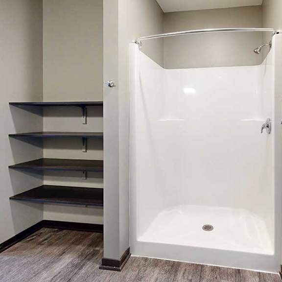 Thumbnail 25 of 51 A walk-in shower with a white surround and chrome fixtures, with built-in linen shelves to the left.