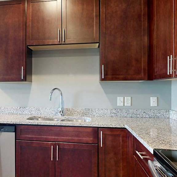 Thumbnail 10 of 51 A stainless steel sink in a modern kitchen with dark wooden cabinets and granite counters.