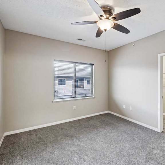 Thumbnail 16 of 25 Apartment bedroom featuring neutral carpeting, a ceiling fan with light, and a window overlooking the exterior.
