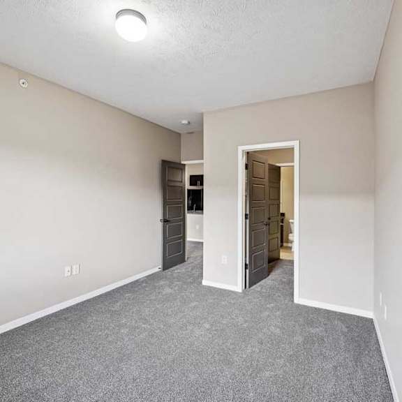 Thumbnail 9 of 25 A room with a grey carpet and a door leading into the bathroom
