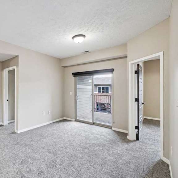 Thumbnail 22 of 25 A spacious room with a carpeted floor and a sliding glass door leading to a balcony.