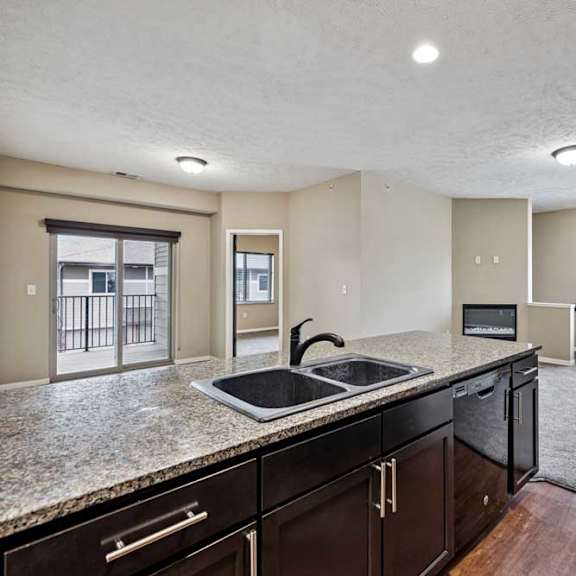 Thumbnail 18 of 25 Apartment kitchen with granite countertops and dark cabinetry, opening into a spacious living area with large windows and sliding doors to a balcony.