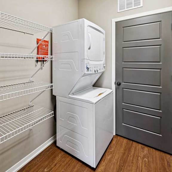 Thumbnail 8 of 25 In-unit laundry area with stacked washer and dryer, built-in wire shelving, and wood-style flooring.