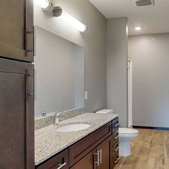 Thumbnail 27 of 33 A long bathroom with a granite vanity sink, mirror, tall cabinet, and walk-in shower..