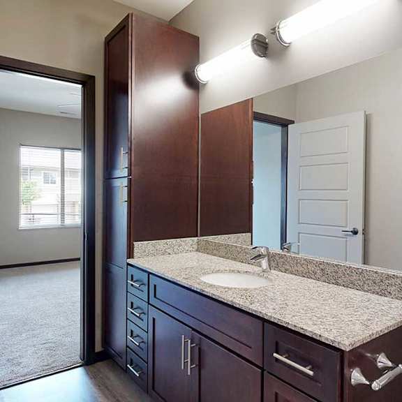 Thumbnail 26 of 33 A long bathroom with a granite vanity sink, mirror, and tall cabinet.