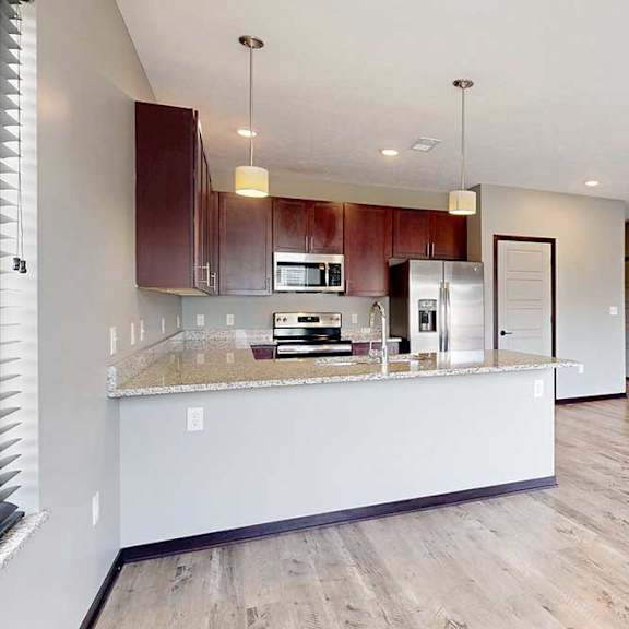 Thumbnail 9 of 33 An open concept living room next to a kitchen with wooden cabinets and a peninsula countertop.