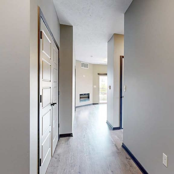 Thumbnail 3 of 33 A hallway leading from the front door to the living room, with a laundry closet on the left, and an adjacent hallway leading to the second bedroom.