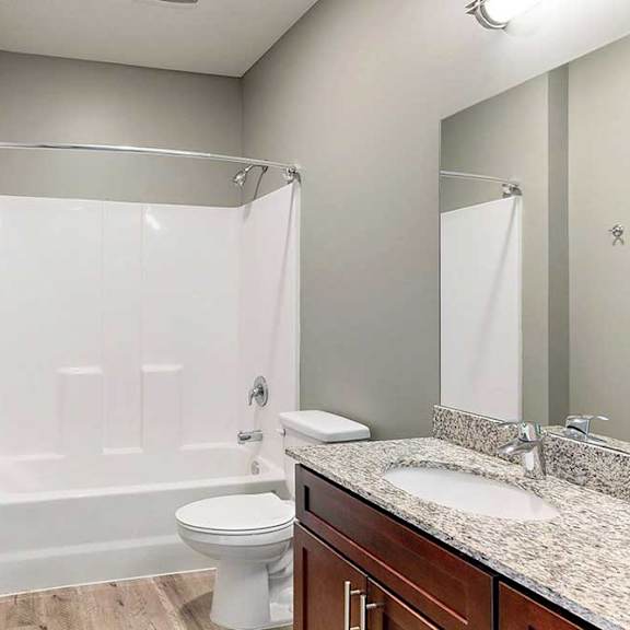 Thumbnail 32 of 33 A bathroom with a granite vanity sink, and a white tub shower with a curved curtain rod.