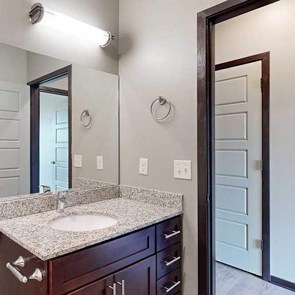 Thumbnail 31 of 33 A bathroom with a granite vanity sink, mirror, overhead light fixture, and a towel ring.