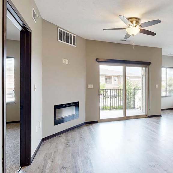 Thumbnail 5 of 33 A living room with a ceiling fan, an electric fireplace, a sliding glass door to a balcony, and wood-style flooring.