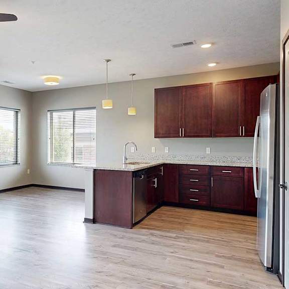 Thumbnail 6 of 33 An open concept living room with a sliding glass door to a balcony, kitchen with wooden cabinets, and a dining area in the background.