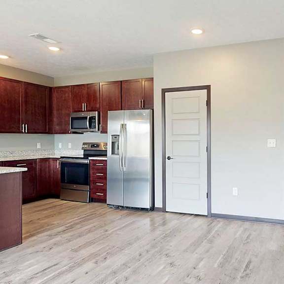 Thumbnail 12 of 33 An open-concept kitchen with wooden cabinets and living room with LVT hardwood flooring.