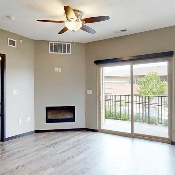 Thumbnail 17 of 33 A living room with a ceiling fan, an electric fireplace, a sliding glass door to a balcony, and wood-style flooring.