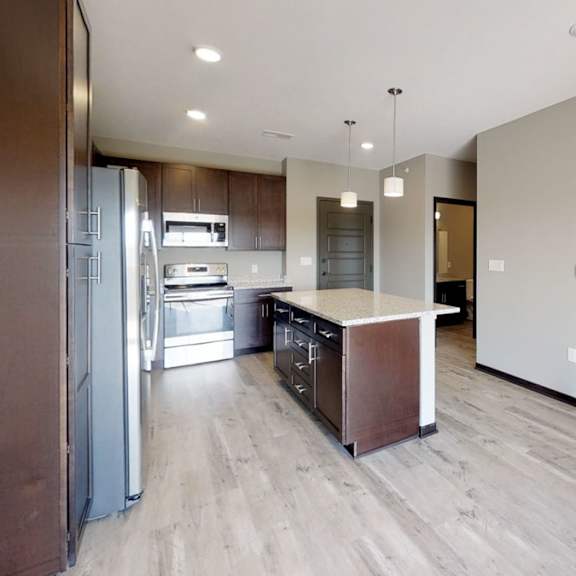 Thumbnail 5 of 10 A modern kitchen with a refrigerator, island, and warm brown cabinets