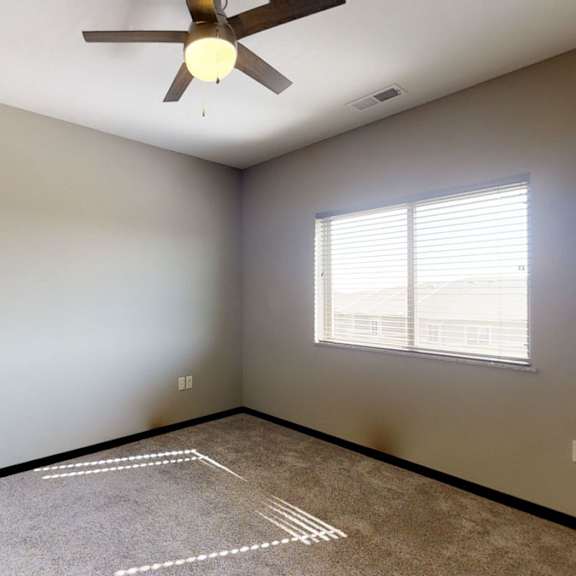 Thumbnail 7 of 10 An empty bedroom with a ceiling fan and a window with blinds.