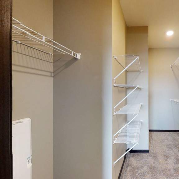 Thumbnail 9 of 10 A walk-in closet with white shelving and a carpeted floor.
