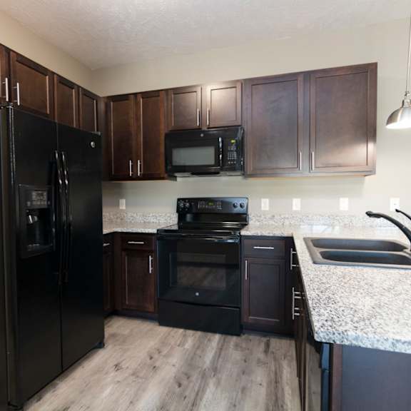 Thumbnail 6 of 14 A black refrigerator stands in a kitchen with wooden cabinets.