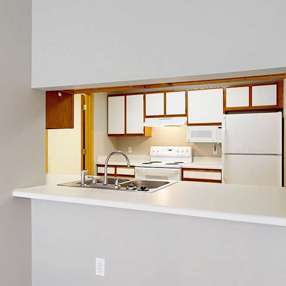 Thumbnail 12 of 29 A galley-style kitchen with white appliances and a breakfast bar with room for seating