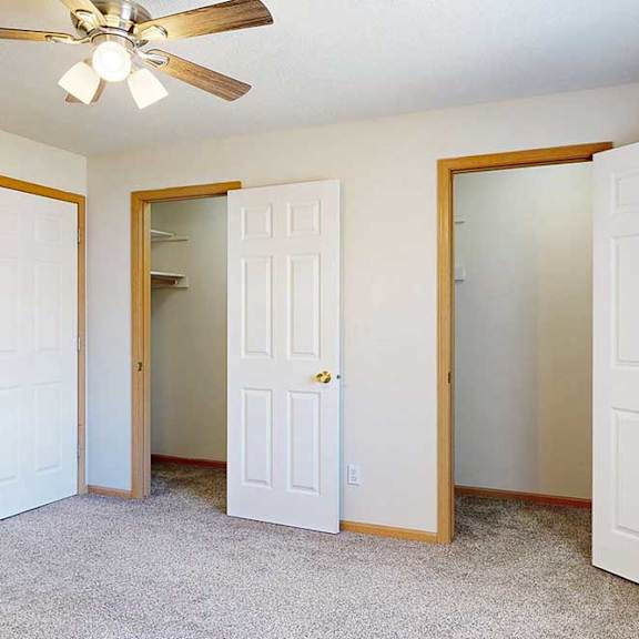 Thumbnail 18 of 31 a carpeted bedroom with ceiling fan and two walk-in closets