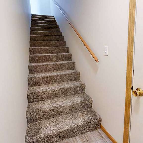 Thumbnail 30 of 31 a carpeted staircase with a wood handrail, and a door to the attached garage