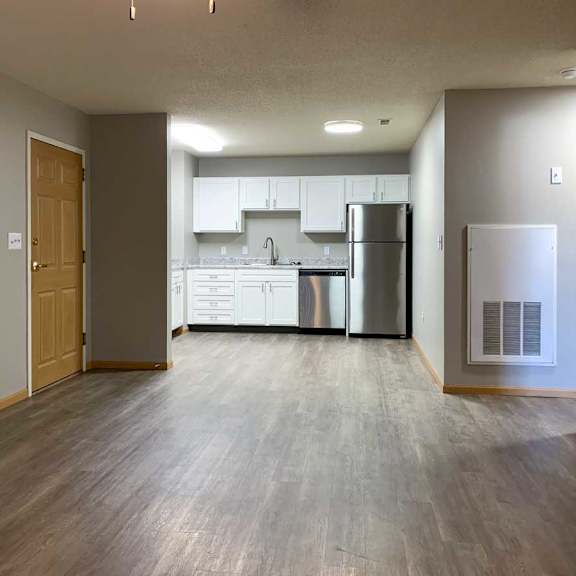 Thumbnail 2 of 21 a living room with hardwood floors next to a kitchen with white cabinets and stainless steel appliances