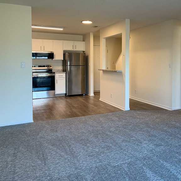Thumbnail 10 of 16 a living room the runs into a kitchen with hardwood floors, stainless steel appliances and white cabients