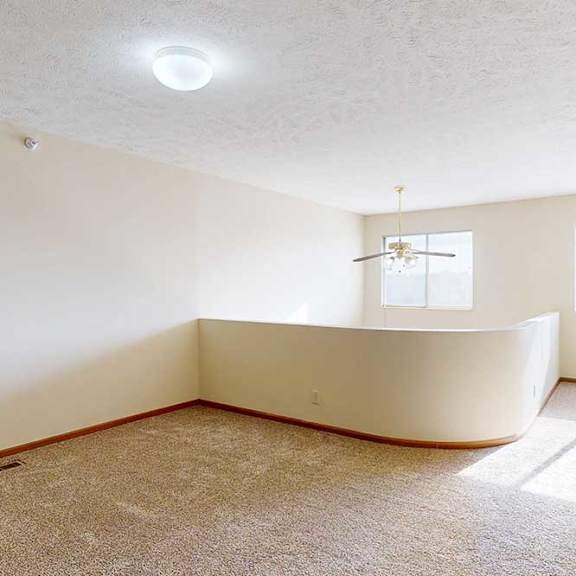 a carpeted loft bedroom with a view open to below, two bright windows, and a ceiling fan.