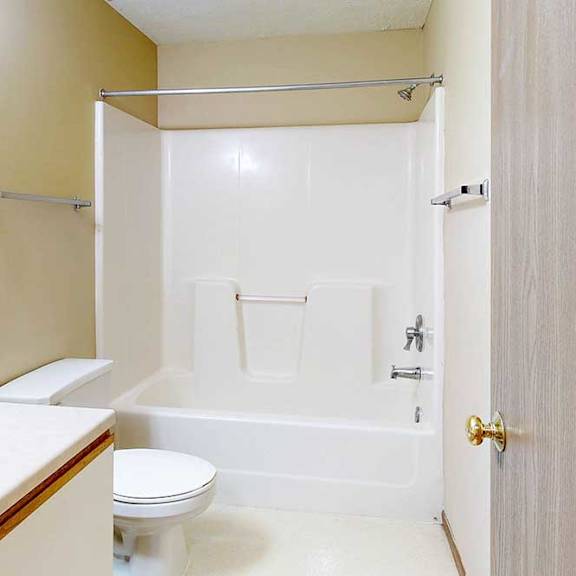 a bathroom with a white and oak vanity sink, tall mirror, towel rack, and combination shower and tub.