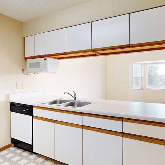 a galley kitchen with white cabinets with oak trim, white appliances, a double-basin sink, and a pass-through window countertop.