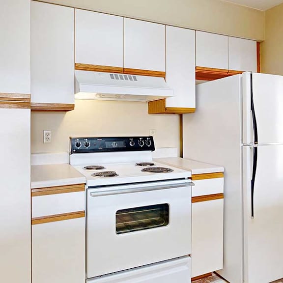 a galley kitchen with white cabinets with oak trim, and white appliances.
