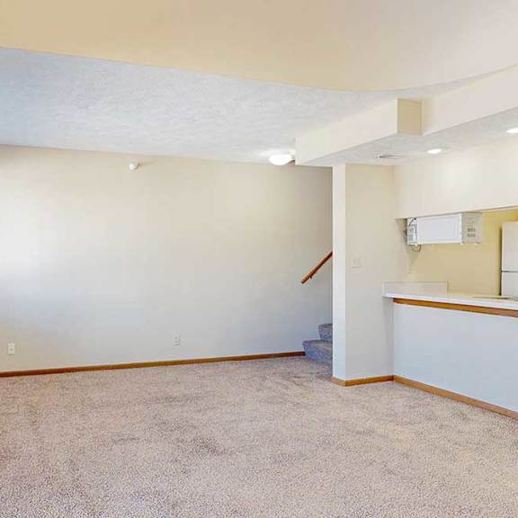 Thumbnail 12 of 33 A carpeted living room with a window, access to the kitchen via a pass-through window countertop, and a staircase to the upper loft area.
