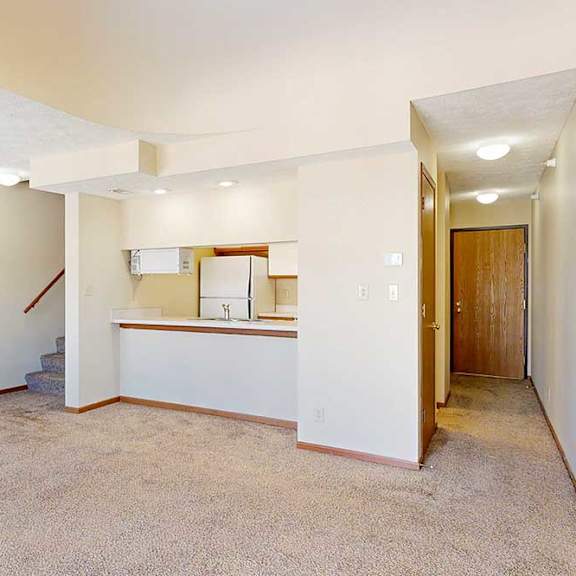 Thumbnail 11 of 33 A carpeted living room with access to the kitchen via a pass-through window countertop, and a staircase to the upper loft area.
