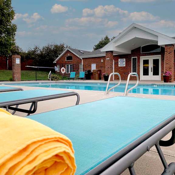 apartment swimming pool with two light blue lounge chairs a clubhouse in the background