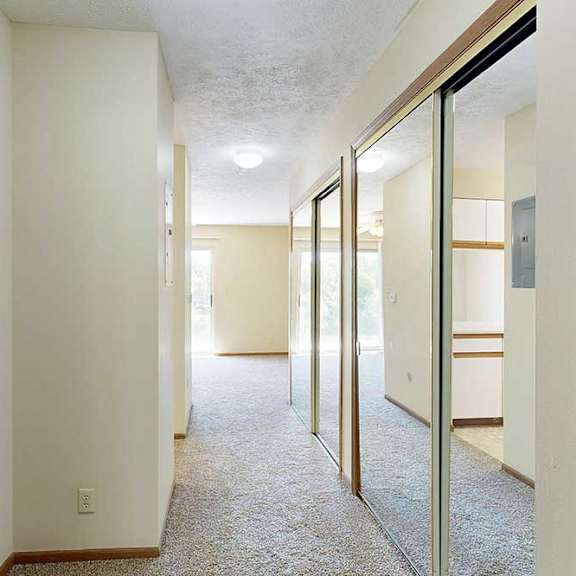 Thumbnail 2 of 21 A hallway to the kitchen and living area, with two sliding mirror door closets on the right.
