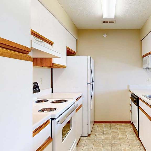 Thumbnail 5 of 21 A galley kitchen featuring white cabinets with oak trim, white appliances, and a passthrough countertop window.