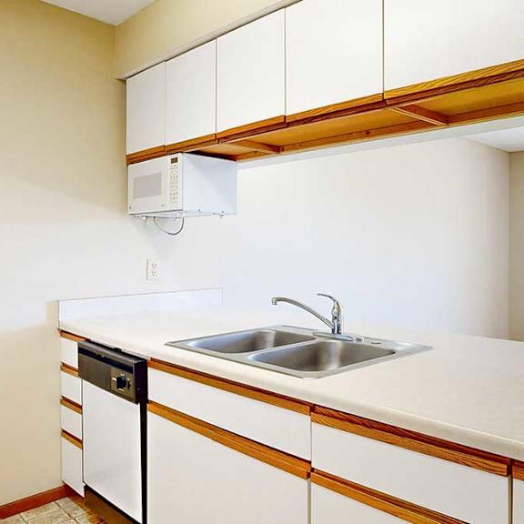 Thumbnail 4 of 21 A galley kitchen featuring white cabinets with oak trim, a double basin sink, a mounted microwave, and a passthrough countertop window.