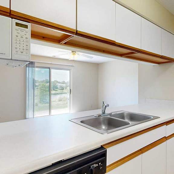Thumbnail 8 of 21 A galley kitchen featuring white cabinets with oak trim, a double basin sink, a mounted microwave, and a passthrough countertop window.