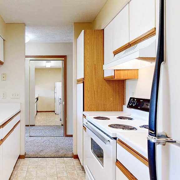 Thumbnail 7 of 21 A galley kitchen featuring white cabinets with oak trim, white appliances, and a passthrough countertop window.