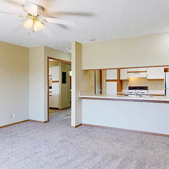 Thumbnail 9 of 21 A living area with a ceiling fan and a view of the kitchen with white and oak cabinets.