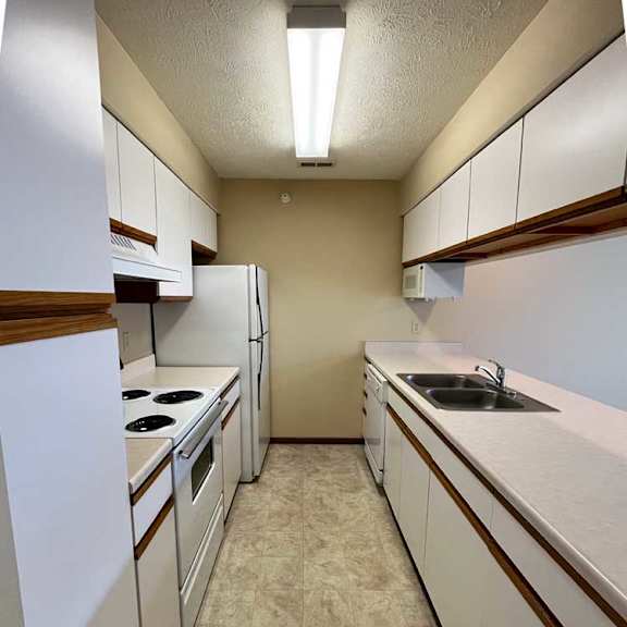 Thumbnail 3 of 13 a galley kitchen with white appliances and brown trim