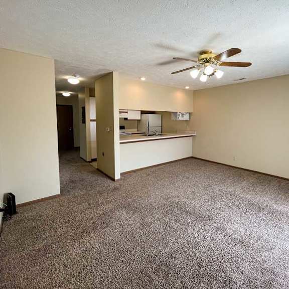 Thumbnail 9 of 13 a living room with a ceiling fan and carpeted floor next to a window to the kitchen