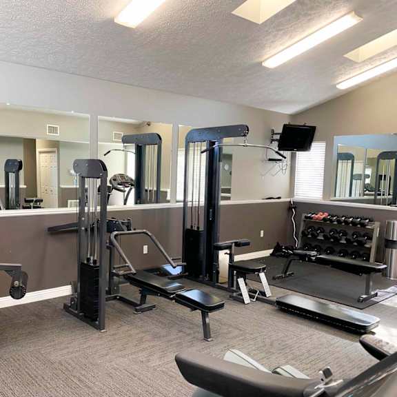 a gym with equipment and mirrors in apartment clubhouse