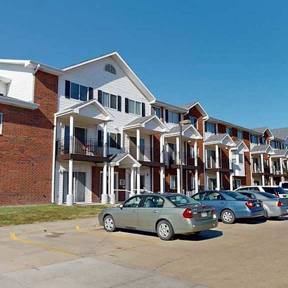 a red brick building with white pillars and siding in front of a parking lot