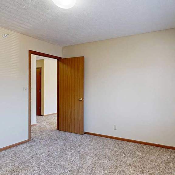 Thumbnail 27 of 29 A bedroom with a carpeted floor, a window with blinds, and a wooden door.