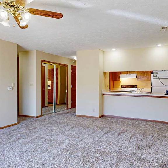 Thumbnail 23 of 29 A living room with a ceiling fan and carpeted floor, with a passthrough countertop to the kitchen.
